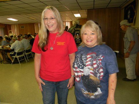 Woman in red, standing beside woman in blue, both are smiling