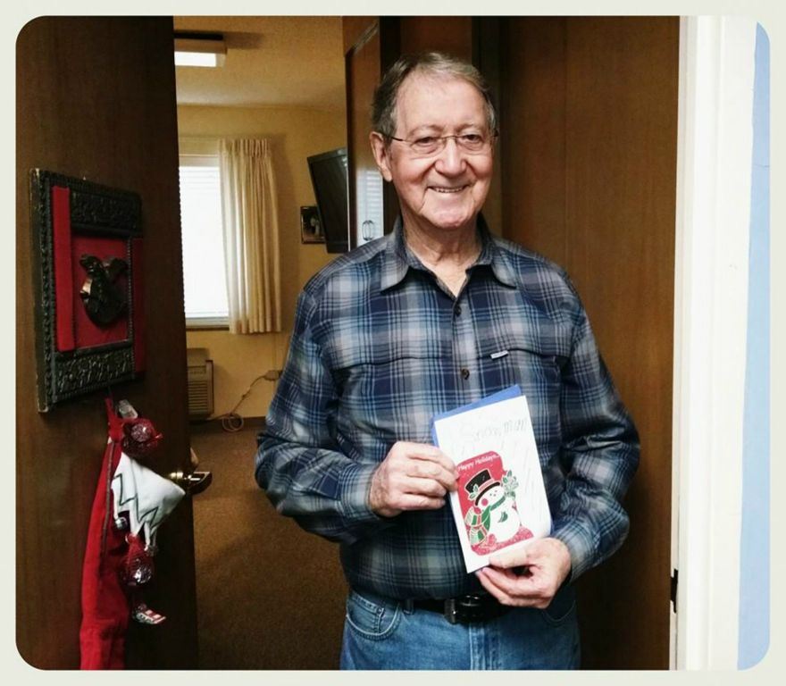 Man in blue plaid smiles at the door holding up a snowman card