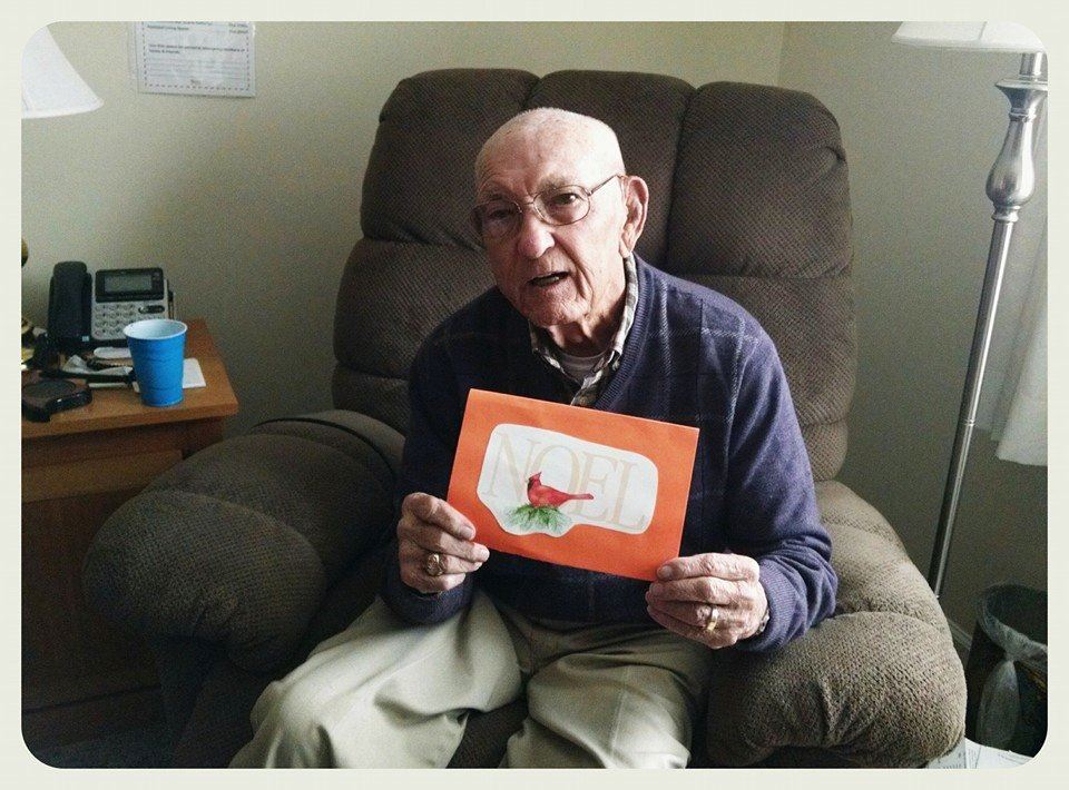 Sitting veteran holds up card with noel and cardinal on front