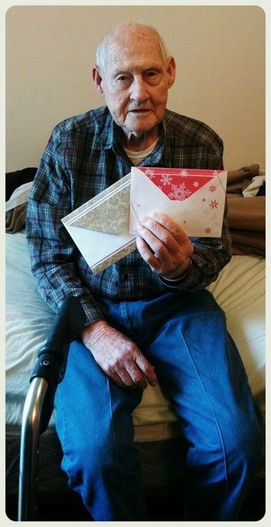 Veteran in blue plaid and jeans sits on edge of bed, holding up two envelopes