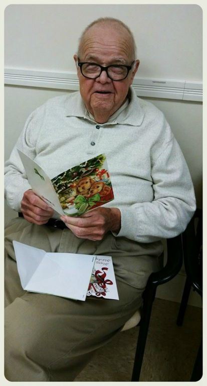 Veteran with glasses sits holding card, looking into and smiling at camera