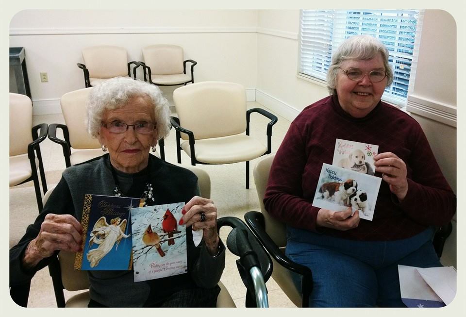 Two women veterans sit holding up cards for the camera
