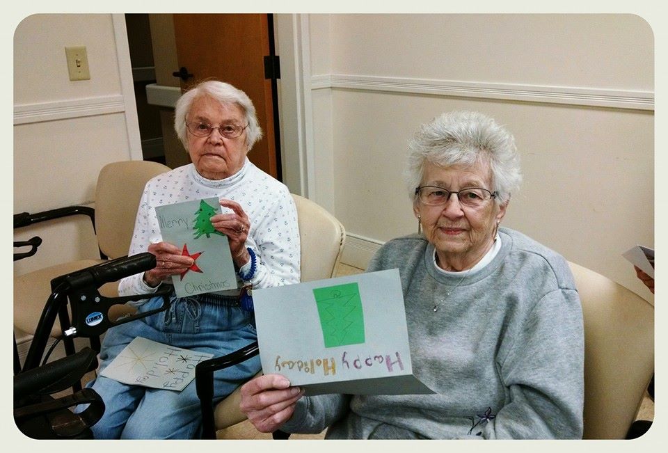 Two sitting woman veterans look at the camera while opening cards