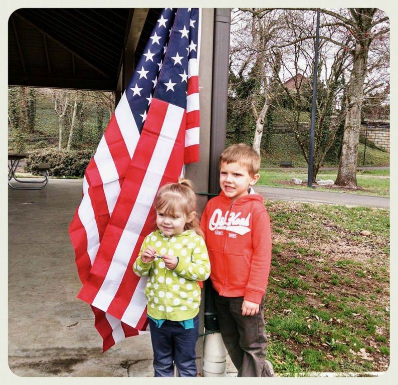Two children stand in front of American flag