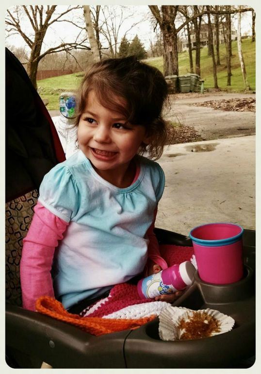 Toddler sitting in stroller smiles, looking away from camera, holding bubbles