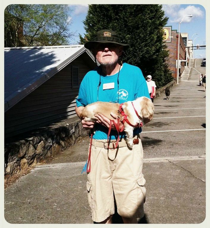 Man in blue shirt and hat carries puppy in arms, walking down street