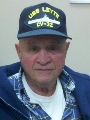 Up close image of older man wearing USS Leyte hat, looking into camera