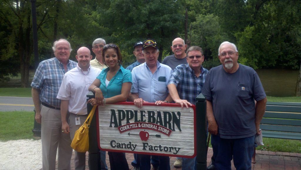 Nine people stand behind wooden siagn with text Applebarn Candy Factory