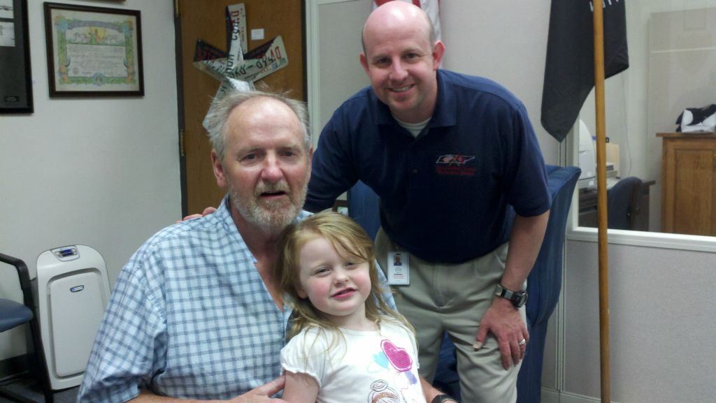 Young girls sits on lap of man in plaid shirt, while Nathan Weinbaum leans in smiling for picture