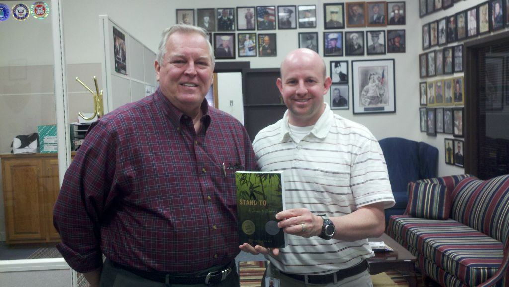 Man in red plaid stands with Nathan Weinbaum in office, Nathan is holding book titled Stand To