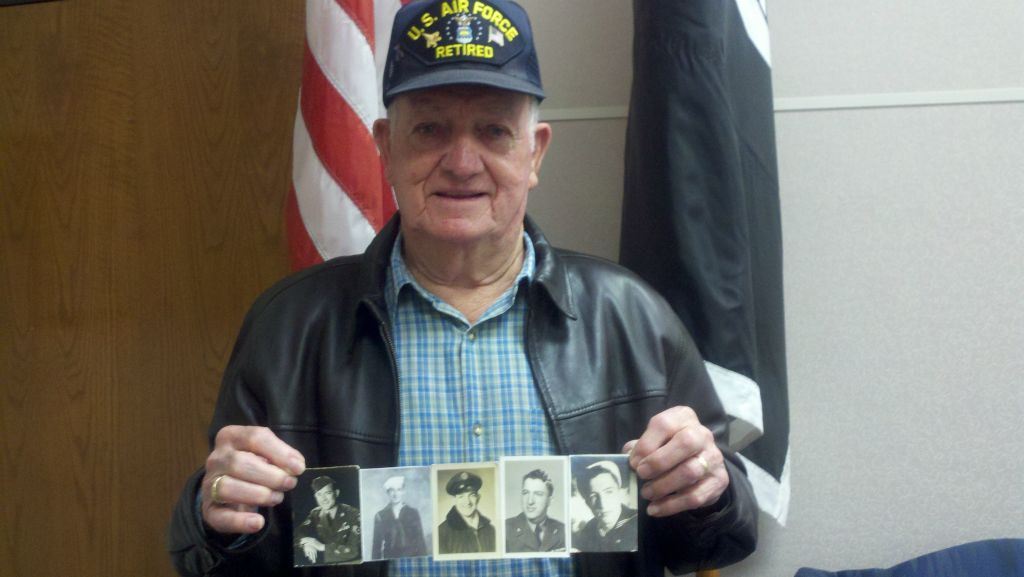 Man wearing US Air Force Retired and blue plaid shirt holds up collage of sepia and black and white photos