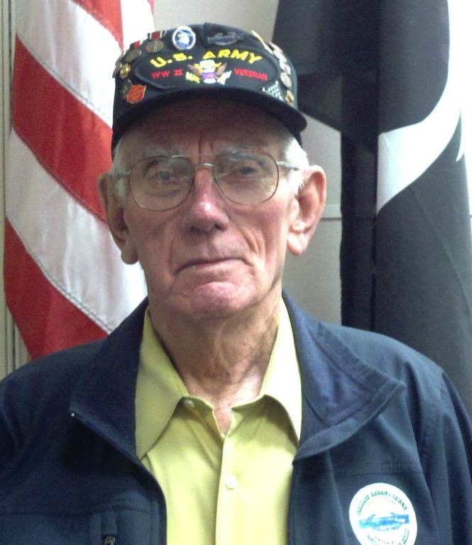 Man wearing yellow shirt and US Army WWII Vet hat looks into camera