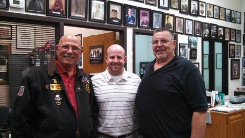 Three men stand together for picture at Veterans Affairs office, looking into camera smiling