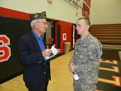 Older gentleman talks to young active duty soldier in uniform in a gym