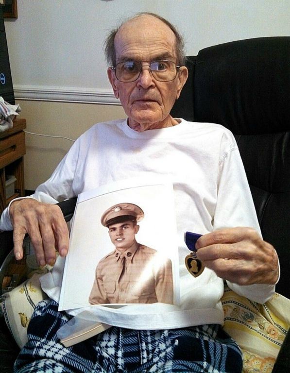 Up close image of veteran wearing white shirt and glasses, sitting in chair, holding sepia self-portrait and purple heart medal