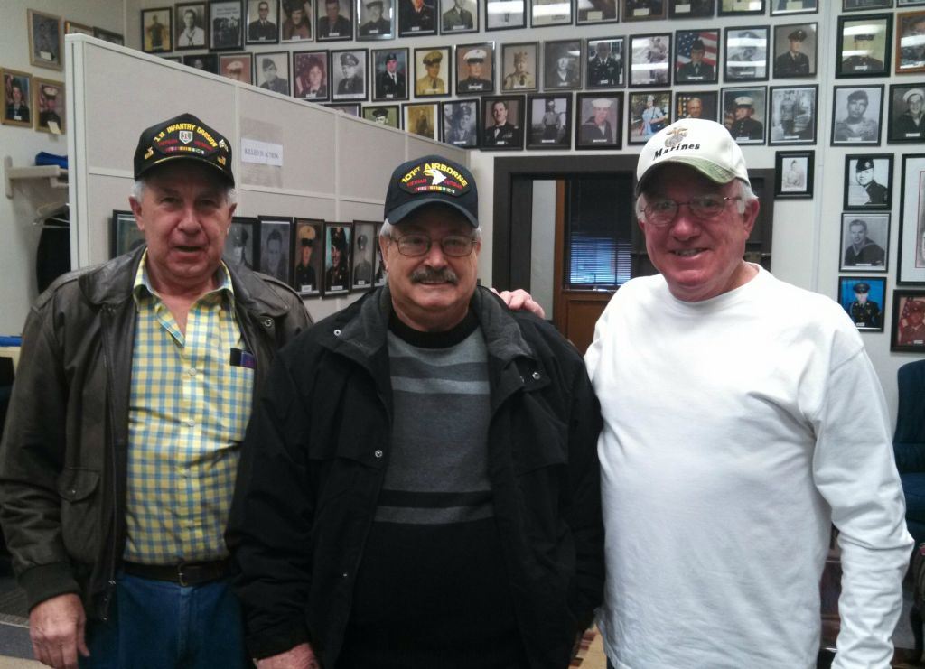 Three men stand together smiling, wearing hats 1st Infantry, 101st Airborne, and Marine