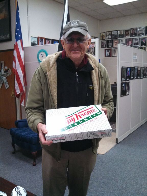 Man in Veterans Affairs office smiling, holding our Krispy Kreme doughnuts box