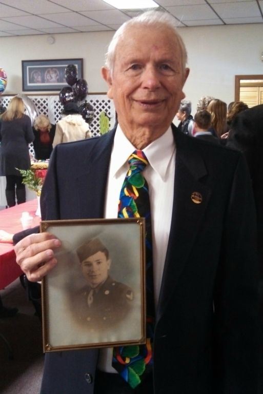 Man wearing navy suit and patterned tie holds up sepia tone military portrait