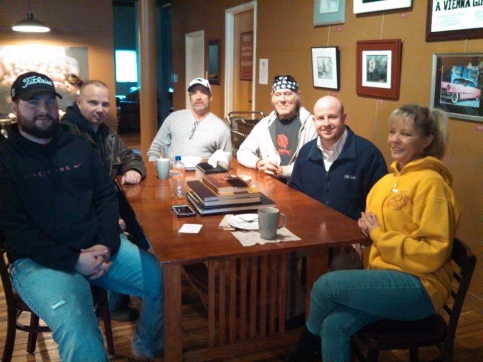 Six people sit atr a wooden table, smiling for the camera