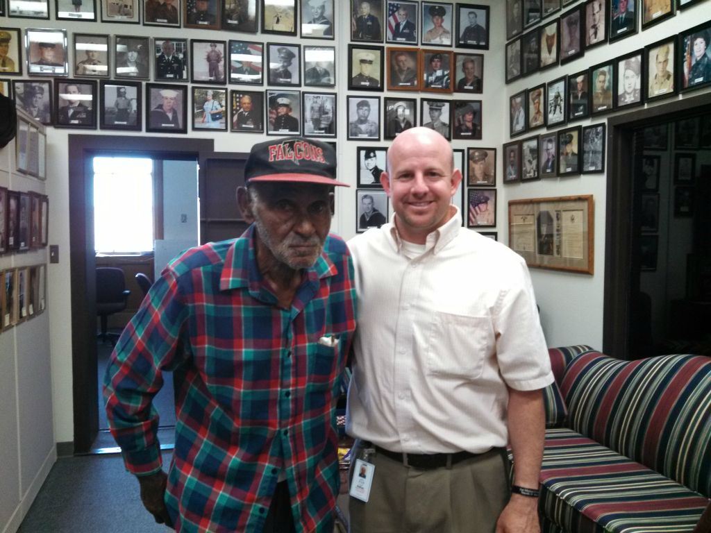 Image of Nathan Weinbaum side hugging man in plaid shirt, at the Veterans Affairs office, both are looking into the camera smiling