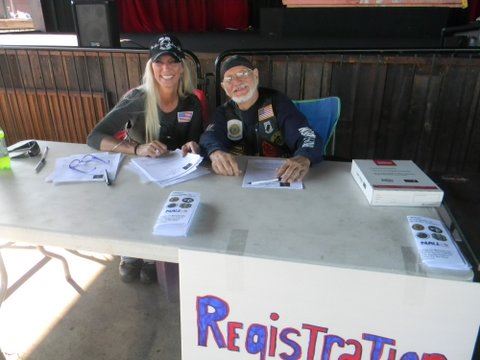 Woman in black shirt and black hat smiles with man in black shirt and black hat, sitting behind registration table