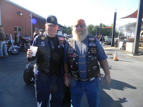 Two men stand outside in arking lot, smiling at camera