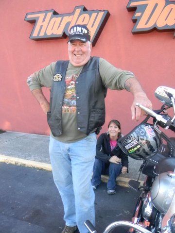 Man smiles at camera, standing with hand on motorcycle handle