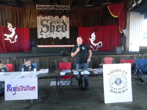 Man in black shirt stands behind table with brochures and pamphlets with microphone