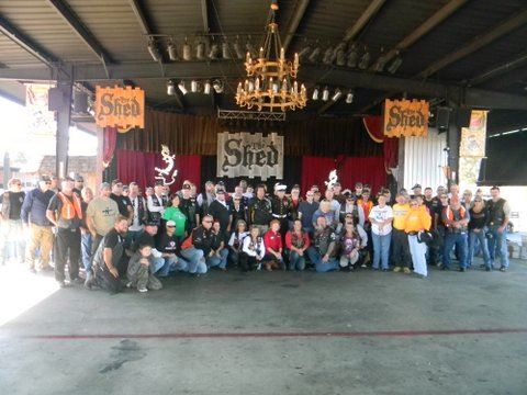 Participants in the drive grouped together smiling for camer in large warehouse type building called The Shed