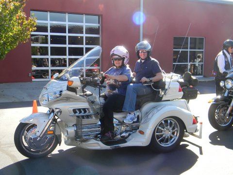 White motorcycle with two riders in front of red building