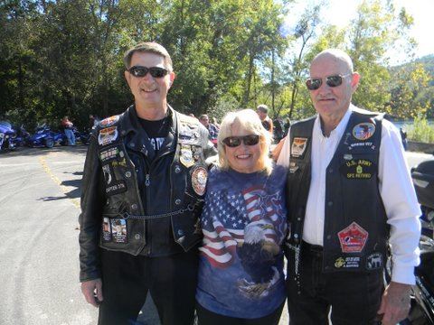 Group of three, two men and one woman standing together in a parking lot looking into the camera smiling