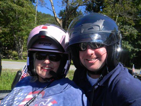 Woman in helmet smiles at camera with man in helmet behind her