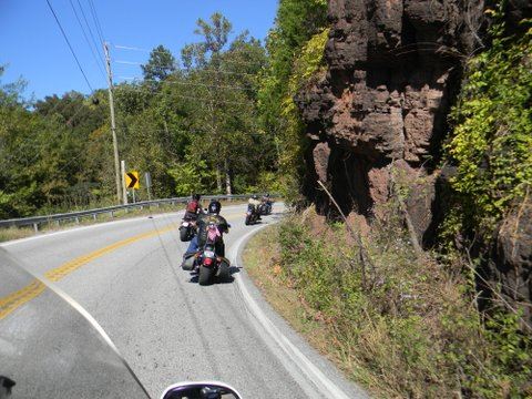 Line of motorcycles driving on street going around a curve with a hill