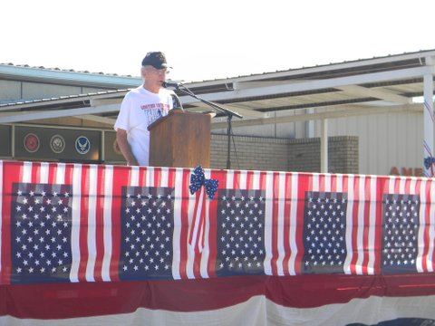 Man in white United Veterans Ride t-shirt, speaking at podium