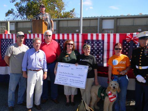 Seven people and service dog in group, smiling for camera, two women are holding oversized check