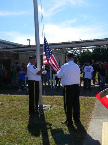 Two men in uniform attach the Missing in Action - Prisoner of War flag to pole