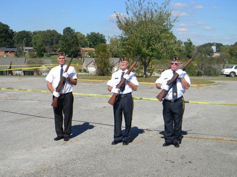 Three men in white shirts with black pants, holding rifles to their chests